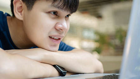 Online studying concept the young boy resting his chin on his arms staring at the laptop, having no ideas to continue his work which make him bored to work right now.の写真素材