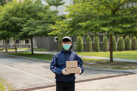 Parcel delivery concept the young sender lifting two boxes of parcels and standing in middle of narrow street to look for building that he will drop these two parcels.の写真素材