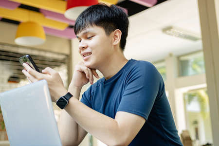 Online studying concept the young man in deep blue T-shirt and black watch using his smartphone to...