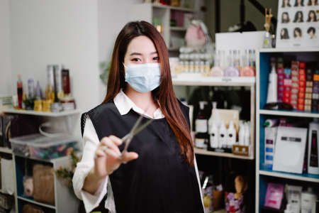 Hair salon concept a pretty hairdresser posing with scissers in a hand  in her hair salon surrounded by haircare products and equipment.の写真素材