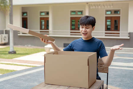 Parcel delivery concept the male teenager feeling awkward and surprised when opening the cardboard box and finding it is empty.の写真素材