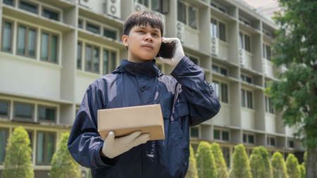 Parcel delivery concept the mail carrier standing in front of the building and calling his customer to confirm the right address for distributing the parcel post.の写真素材