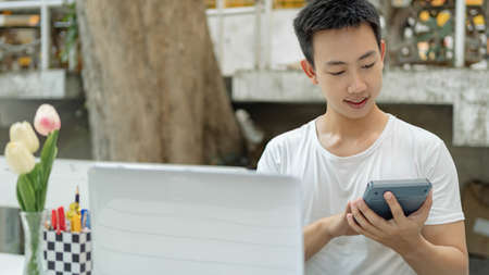 Online studying concept the man in plain white T-shirt feeling quite happy and holding the calculator for calculating numbers in accounting class.の写真素材
