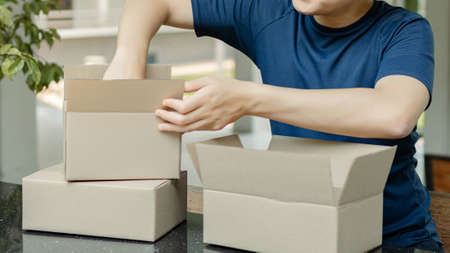 Parcel delivery concept the smart boy wearing the blue t-shirt checking the parcel and the stuffs inside from the online shop on the counter bar.の写真素材