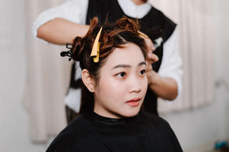 Hair salon concept a male hairstylist using a comb to grab a lock of hair and using hair dryer for drying and straighteningの写真素材