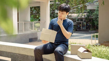 Parcel delivery concept the young man looking disappointed to the stuff in the cardboard box that is not the same to what he saw in the photo.の写真素材