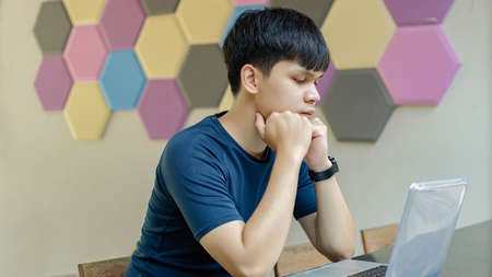 Online studying concept the man wearing dark blue shirt sitting on the wooden chair and trying to come out of a creative idea to be added in his new project.の写真素材