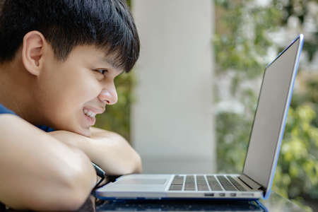 Online studying concept the young boy resting his chin on his arms staring at the laptop, having no ideas to continue his work which make him bored to work right now.の写真素材
