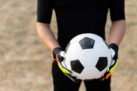 Sports and recreation concept a male teenage goalkeeper wearing black outfit and a pair of colorful gloves holding a soccer.の写真素材
