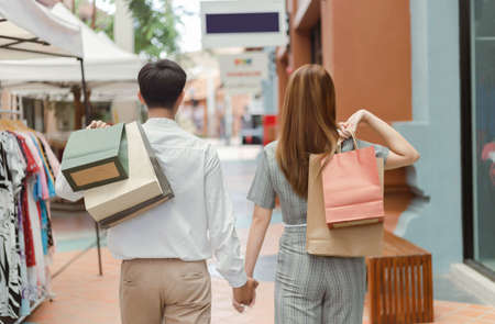 shopping concept Both male and female shoppers holding each otherâs hand and carrying shopping bags on each back while walking past clothes shop.の写真素材