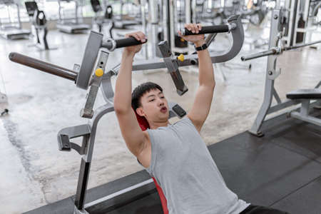 exercise concept The muscly man with earnest face trying to control his breath while lying his back on the weight machine and pulling the weight down.の写真素材