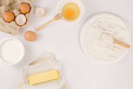 bread concept a stick of butter, a small bowl of raw egg, a plate of flour with a wooden spatula on...