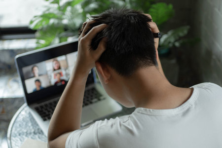 Online studying concept a young college student scratching his hair very hard and looking frustrated and confused after he is late for his online classroom.の写真素材