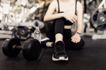 exercise concept The female with dark tone of outfits resting herself on the black carpet floor after playing on the dumbbell beside her.の写真素材