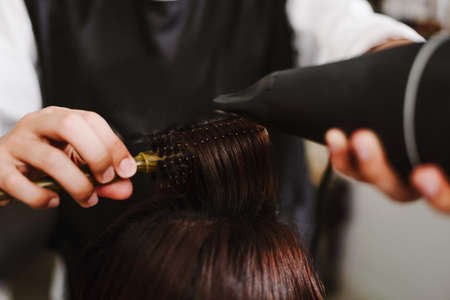 Hair salon concept a male hairstylist using a comb to grab a lock of hair and using hair dryer for drying and straighteningの写真素材