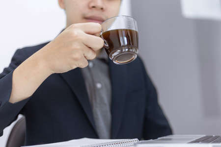 Business partners concept a young male entrepreneur holding a cup of black coffee sitting with a laptop while attending in a monthly meeting.の写真素材