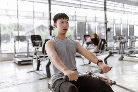 exercise concept The brawny guy in the exercise club paying his attention on the seat roll machine...