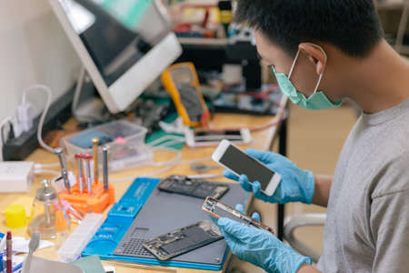 Phone repair concept a male phone repairman wearing gloves and a mask checking the components of the mobile phone.の写真素材