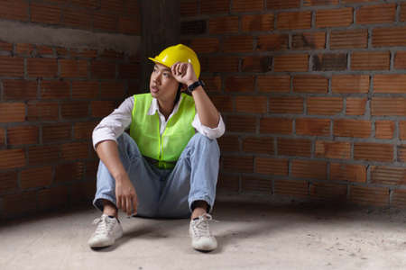 engineer concept The builder sitting at the corner of the building with worried face and staring at the construction work.の写真素材