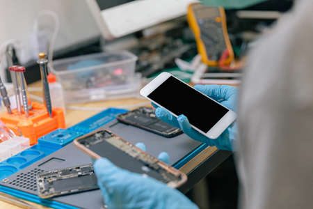 Phone repair concept a male phone repairman wearing gloves and a mask checking the components of the mobile phone.の写真素材
