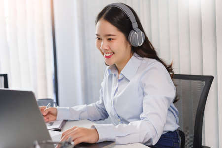 Business concept, Businesswoman in headset to meeting on video conference and taking notes on paper.の写真素材