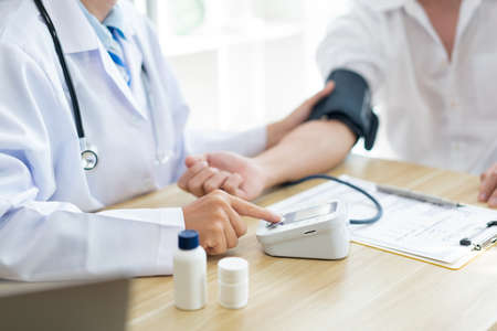 Visiting a doctor concept A doctor sitting using the tool to measure blood pressure on the patientâs arm carefullyの写真素材