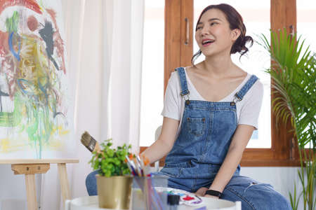 Creative of art concept, Young asian woman hold paint brush and happy to look on art masterpiece.