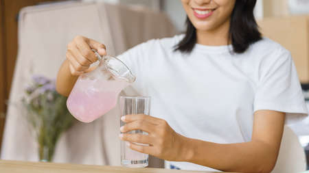 Cozy lifestyle concept, Young woman pour water from jug into glass while having snack at home.の写真素材