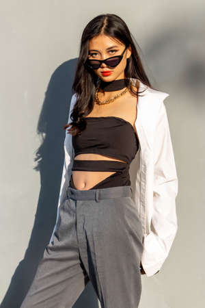 Fashionable concept, Fashion woman to pose in sunglasses and pants with white shirt near gray wall.