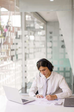 Business concept, Businessman wearing headphone and taking notes information while video conference.の写真素材