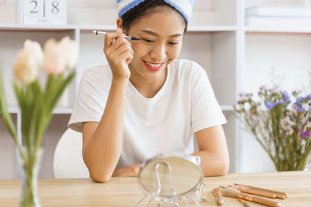 Cozy lifestyle concept, Young woman in turban after shower and apply eyeliner on eyelid for makeup.の写真素材