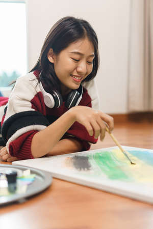 The art concept, Asian female artist lying on the floor and using paint brush to painting on canvas.の写真素材