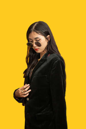 Fashion concept, Fashionable woman wear sunglasses and oversize coat to pose on yellow background.の写真素材