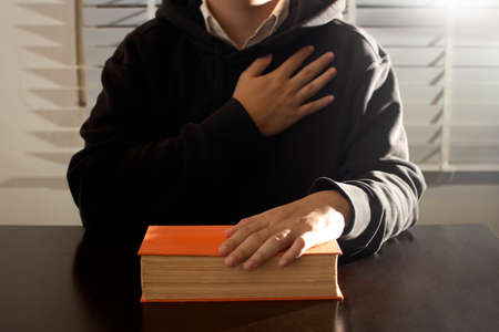 Religion concept, Young asian man put hand on chest for praying to jesus after reads the bible.の写真素材