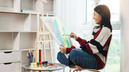 The art concept, Asian female artist sitting on the chair and holding canvas to painting artwork.