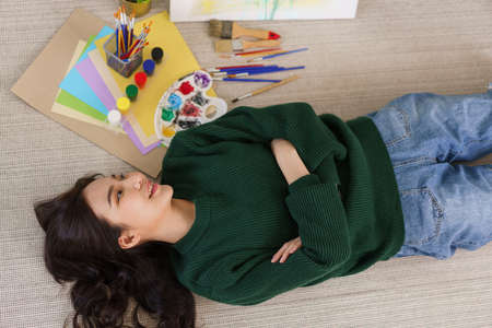 Creative of art concept, Young asian woman lying on the floor with art masterpiece in art studio.