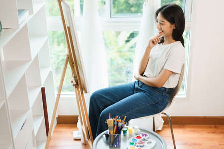 The art concept, Asian female artist sit front of canvas and thinking to create idea for artwork.の写真素材