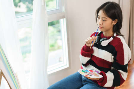 The art concept, Asian female artist sitting front of canvas and thinking to create about artwork.の写真素材