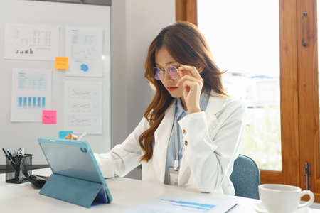 Successful business concept, Businesswoman use hand to holding glasses while writing data on tablet.