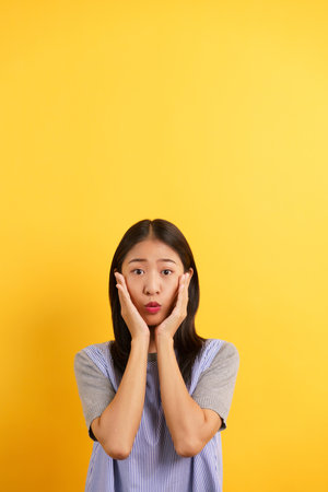 Young women surprised face and touching face with both hands with isolated on yellow background.の写真素材