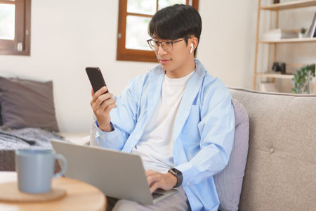 Home office, Businessman wears wireless headphones to meeting on smartphone and working on laptop.の写真素材