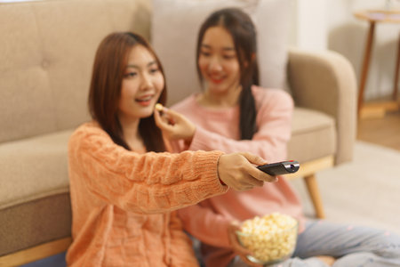 Lifestyle at home concept, LGBT lesbian couple feeding popcorn to girlfriend while watching movie.の写真素材