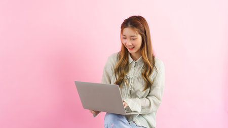 Young women working and typing to chatting with colleague on laptop isolated on pink background.
