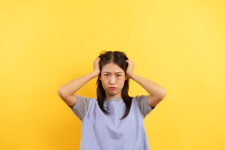Young women angry face and holding head with hands isolated on yellow background.