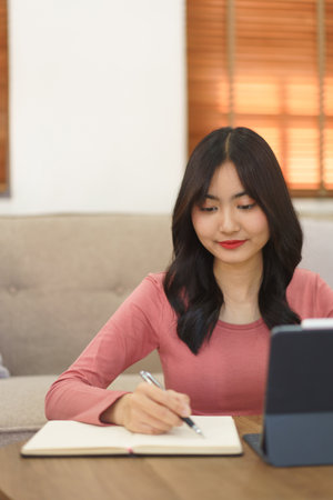 Young businesswoman reading business data on tablet and writing note in paper while working at home.の写真素材