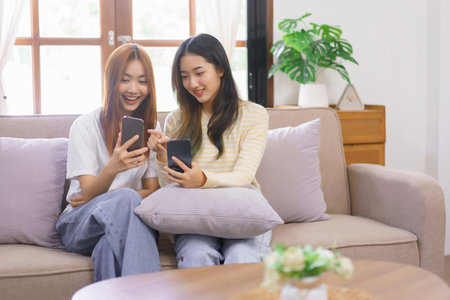 Relax at home concept, LGBT lesbian couple looks on phone and point while shopping online together.の素材