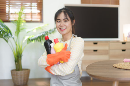 Maid holding cleansing bottles and showing thumb up after cleaning and wiping the dirty in home.の素材