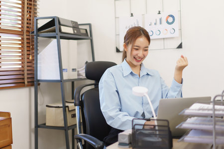 Startup business concept, Businesswomen raise arm in celebrate after receive good news at workplace.の素材