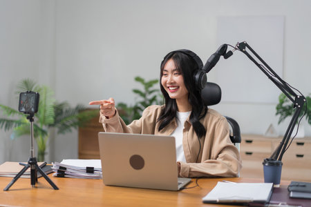 Female podcaster use smartphone and speaking with audience on microphone to recording video podcast.の写真素材
