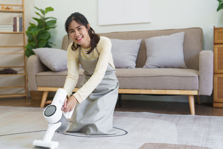 Maid vacuuming on the carpet with handheld cordless vacuum cleaner for cleaning dust in living room.の写真素材